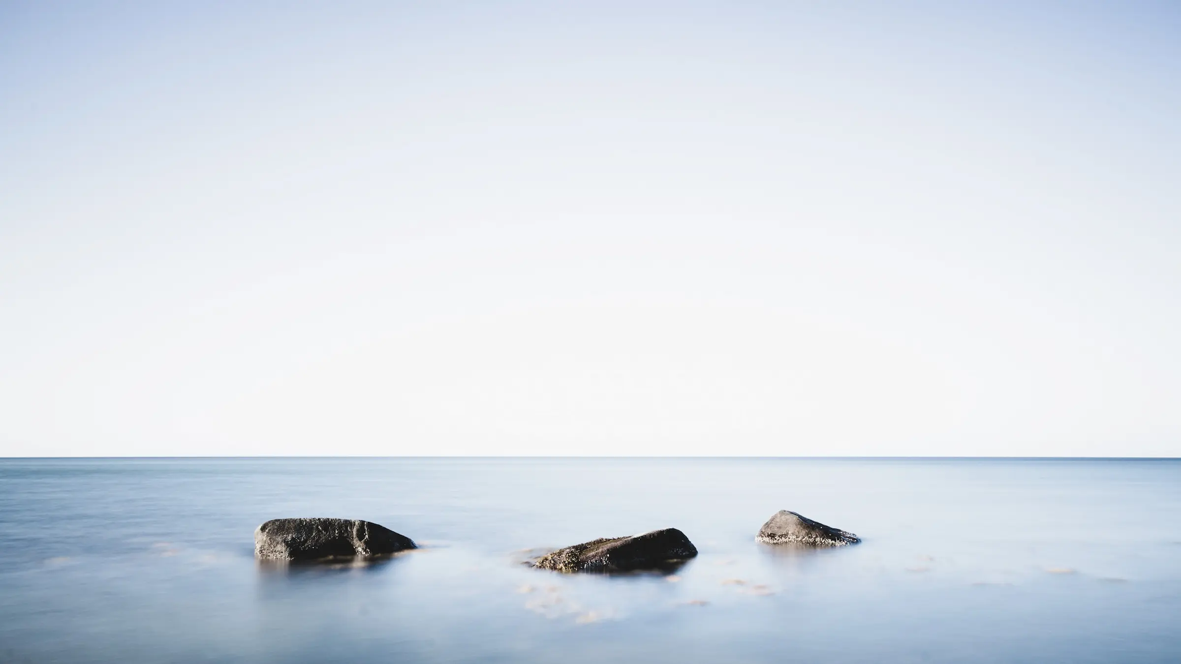 A calm sea beneath an open sky, with three rocks resting in still water